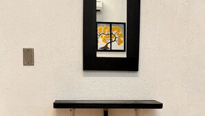A room with a white textured wall, a black-framed mirror, a wooden stool, and a red cylindrical object. - Room in the heart of Cancun (29)