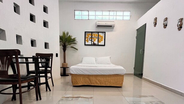 A hotel room with a bed, a desk with chairs, a potted plant, and a wall with square cutouts. - Room in the heart of Cancun (29)
