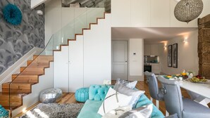 A modern living room with a staircase, a dining area with a table set for breakfast, and a kitchen in the background. - Oporto Platinum Loft // Luxury Accommodation// Unforgettable Douro River View. (Porto)
