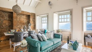 A spacious living room with a stone wall, a teal sofa, and a dining area with a white table and chairs. - Oporto Platinum Loft // Luxury Accommodation// Unforgettable Douro River View. (Porto)