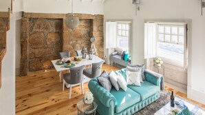 A spacious living area with a stone fireplace, a dining table with chairs, a teal sofa, and large windows offering a view. - Oporto Platinum Loft // Luxury Accommodation// Unforgettable Douro River View. (Porto)