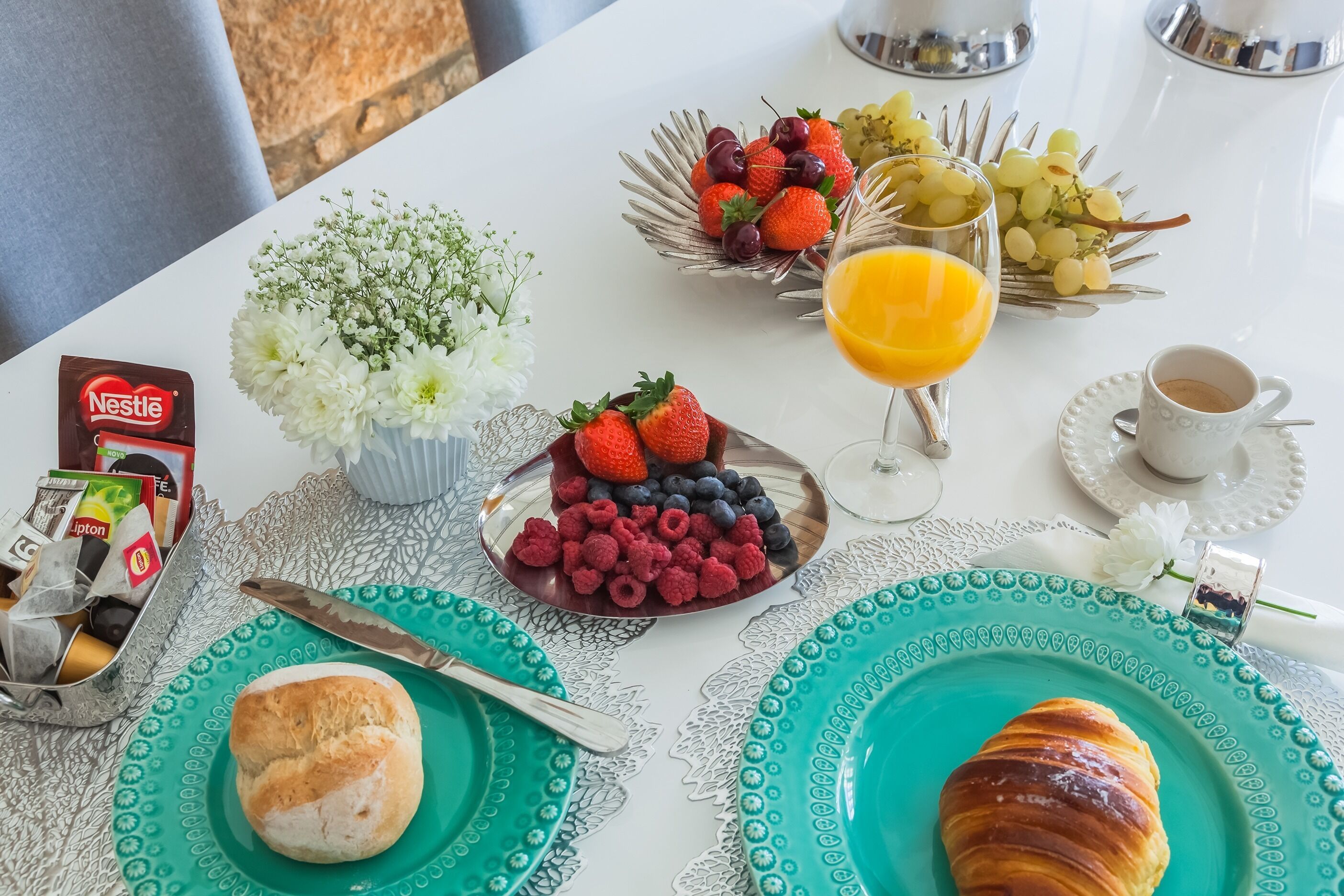 A breakfast table with a croissant, a plate of berries, a glass of orange juice, a cup of coffee, and a vase of flowers.