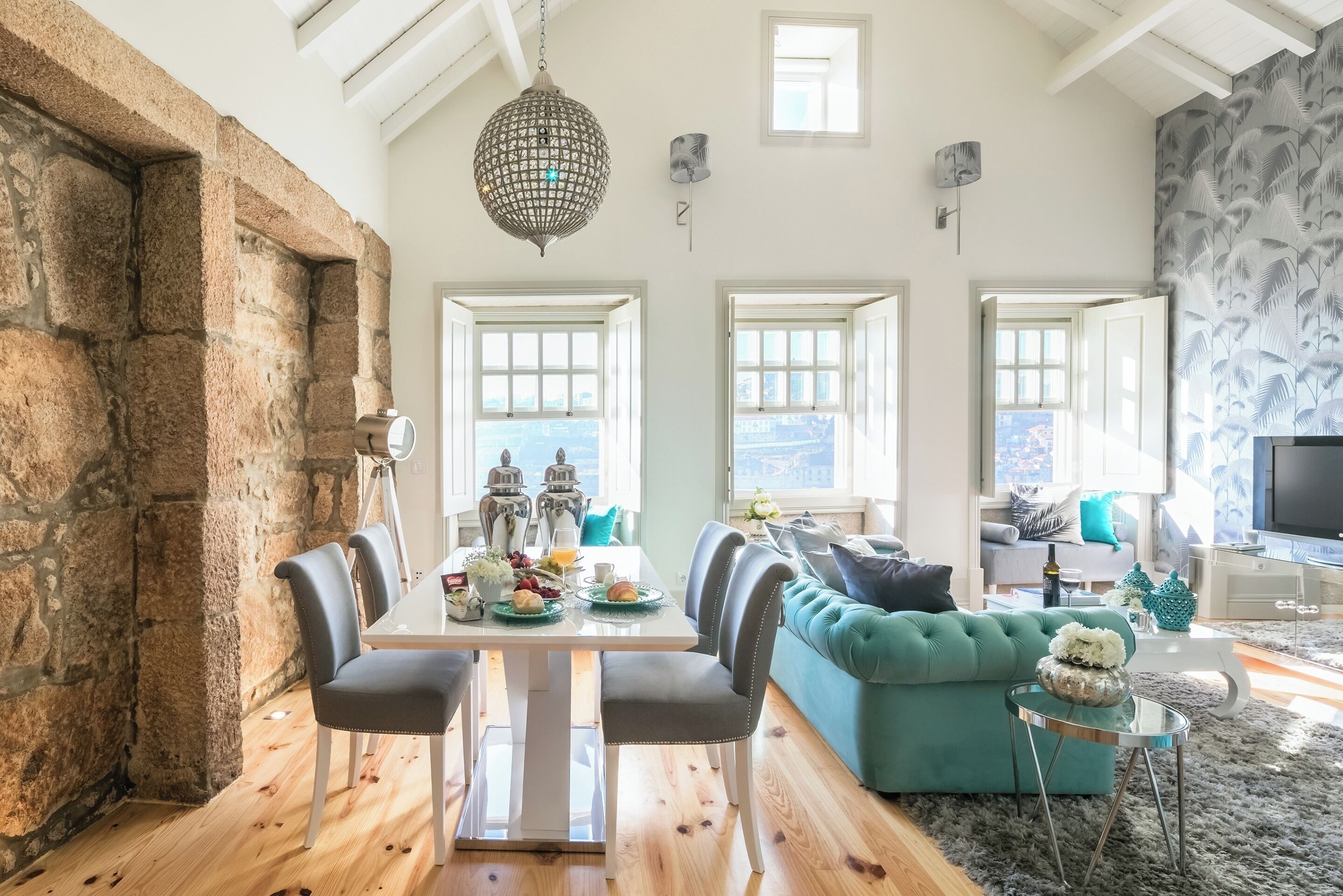 A dining area with a stone wall, a chandelier, and a table set with food and drinks.