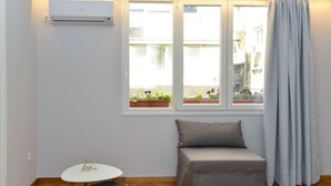 Ein kleines Zimmer mit Fenster, einer Couch, einem kleinen Tisch und einer Klimaanlage.