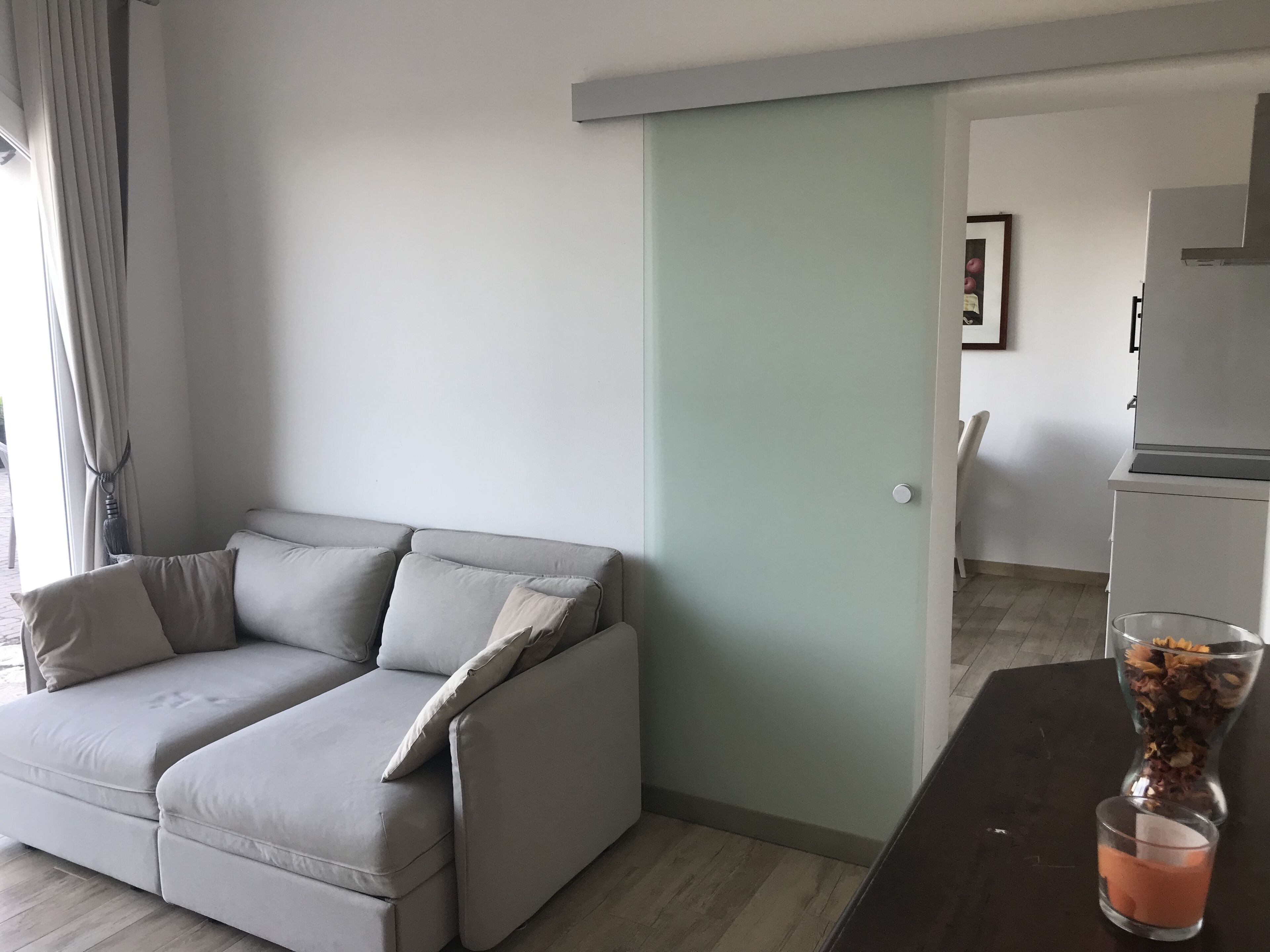 Una sala de estar moderna con un sofá seccional gris, una mesa de centro de vidrio y una mesita con un jarrón de flores secas.