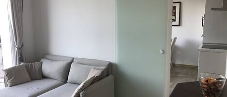 Una sala de estar moderna con un sofá seccional gris, una mesa de centro de vidrio y una mesita con un jarrón de flores secas.