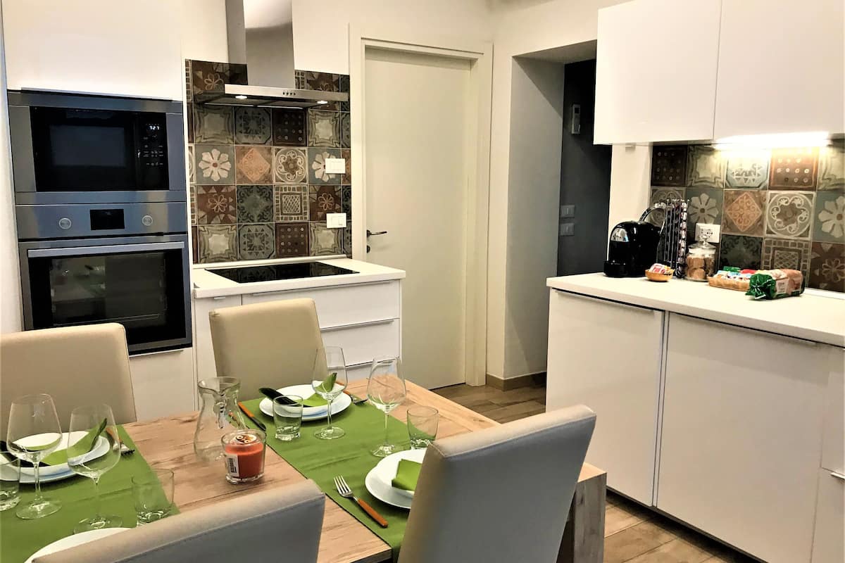 A modern kitchen with a dining area. It includes a built-in oven, microwave, and a coffee machine on the counter.