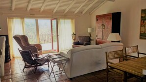 A living room with a sofa, a dining table, and two chairs. There is a window with curtains, a lamp, and a painting on the wall. - Country House with Swimming Pool Large Terrace and an amazing panoramic view (Marvão)