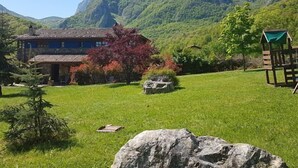 Ein Haus im traditionellen Stil, umgeben von üppiger grüner Landschaft und Bergen im Hintergrund.