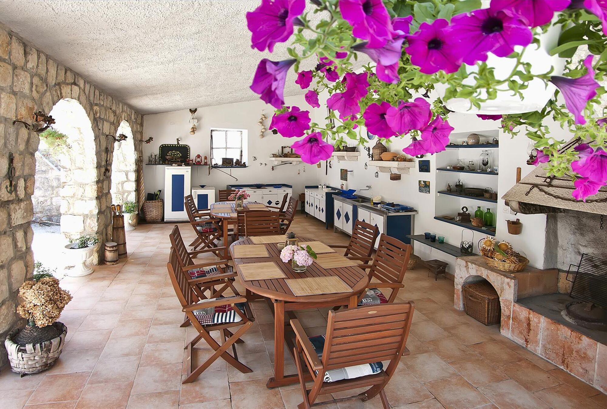 Un coin repas rustique avec un mur en pierre, des meubles en bois et des fleurs violettes suspendues.