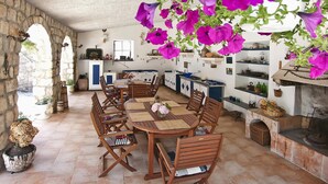 A rustic dining area with a stone wall, wooden furniture, and hanging purple flowers. - Room 5 a/c park view Beach&Sea front Castle parking (Zaton)