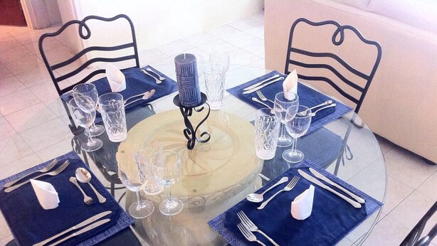 A round glass table with a central cake, surrounded by four chairs with blue napkins and cutlery. - Spacious 2 Bed 2 Bath Condo Across From The Beach (CHRIST CHURCH)