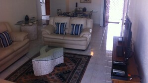 A living room with a sofa, armchairs, a glass coffee table, and a television. - Spacious 2 Bed 2 Bath Condo Across From The Beach (CHRIST CHURCH)