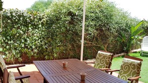 A patio with a wooden table and chairs, surrounded by lush greenery and a small lawn. - Apartment rental, golf and beach // golf and beach Apartment (torre de benagalbon)