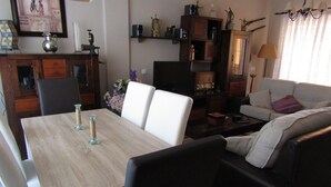 A living room with a wooden dining table, white chairs, a sofa, and a television. - Apartment rental, golf and beach // golf and beach Apartment (torre de benagalbon)