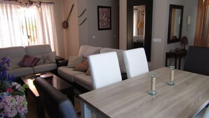 A modern living room with a sofa, a dining table, and a coffee table. There is a chandelier, a painting on the wall, and a mirror. - Apartment rental, golf and beach // golf and beach Apartment (torre de benagalbon)