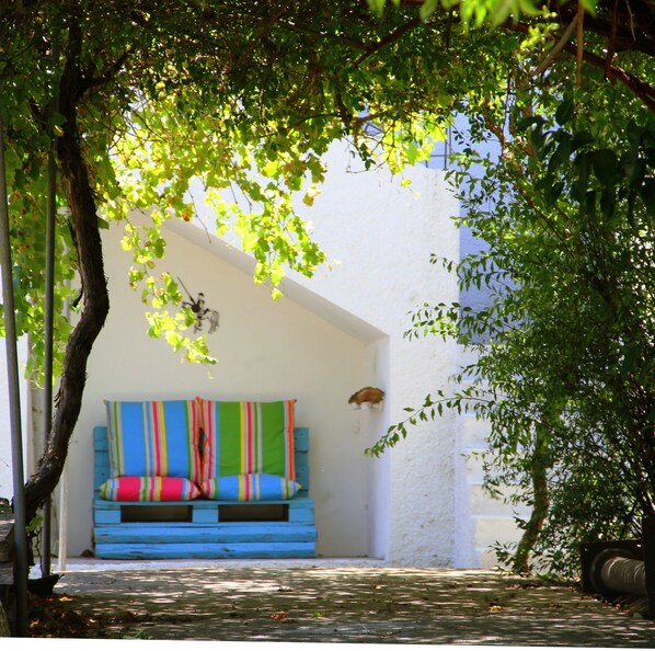 A covered outdoor seating area with colorful cushions and a white wall in the background.
