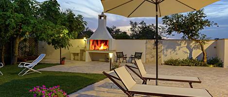 Un patio al aire libre con suelo de piedra, sillones de descanso, una chimenea y una sombrilla.
