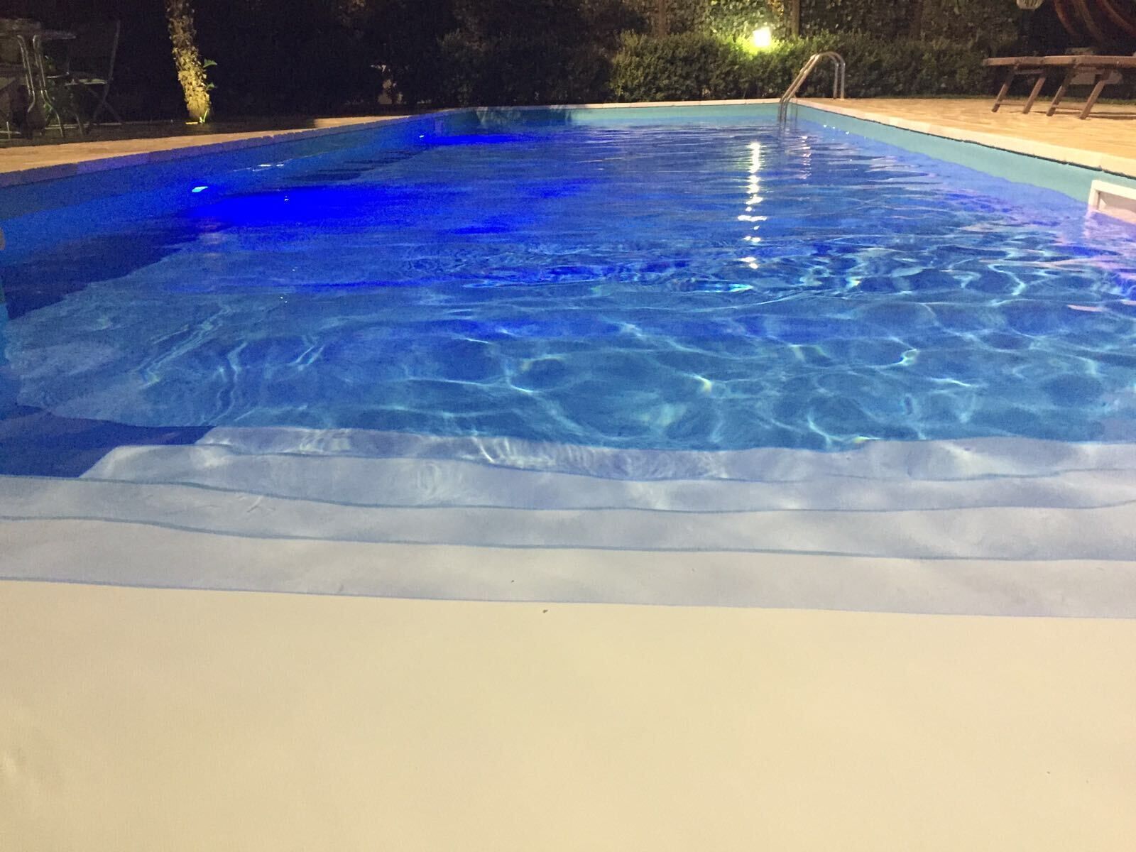 A swimming pool with clear blue water, surrounded by a deck and a night-time setting.