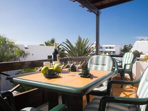 Een terras met een houten tafel en gestreepte stoelen, met uitzicht op een woonwijk met palmbomen en witte gebouwen.
