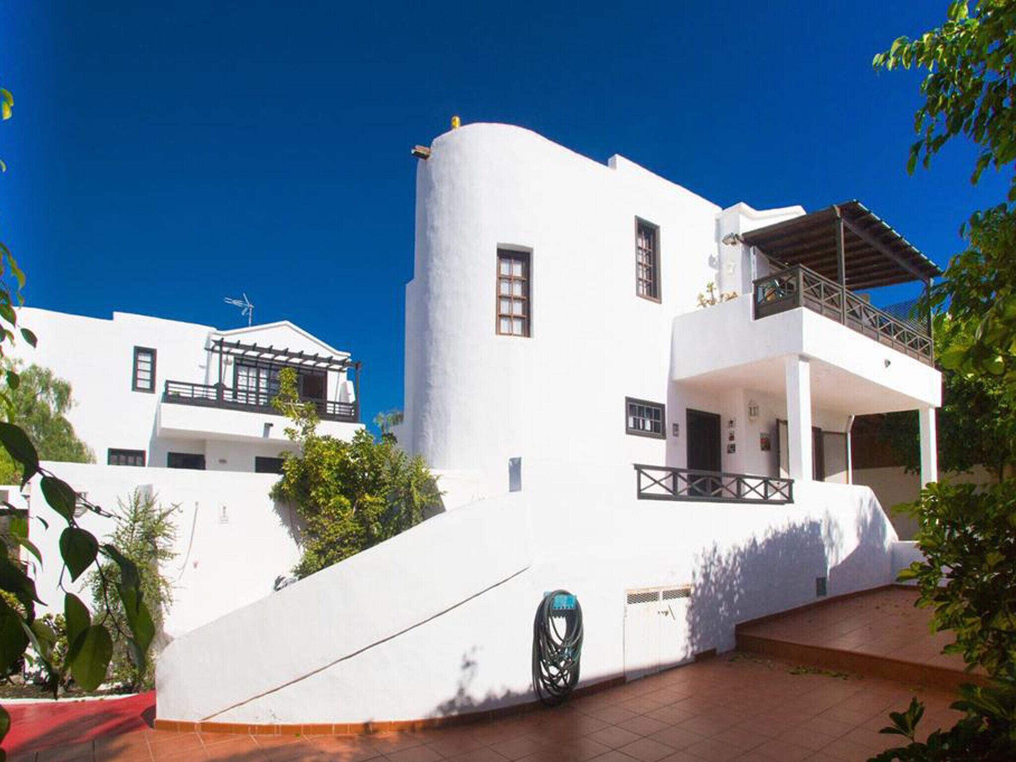 A modern white building with a curved facade, multiple balconies, and a red-tiled entrance.