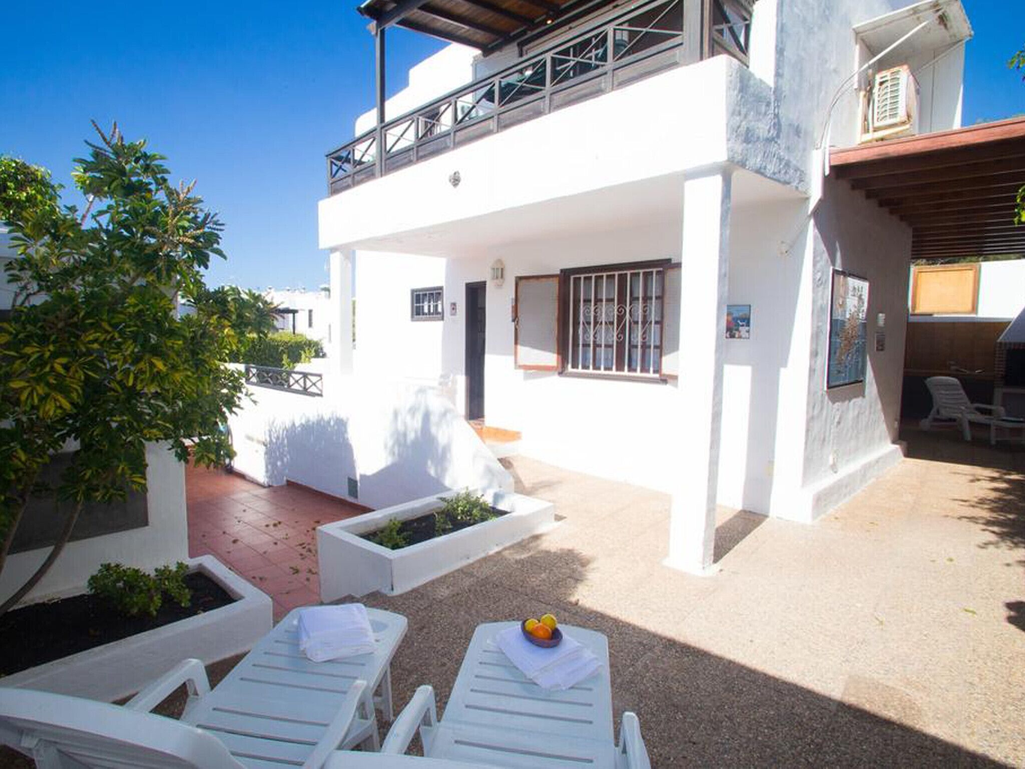 Un bâtiment blanc doté d’un balcon, d’un espace extérieur aménagé pour s’asseoir et d’un petit jardin.