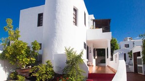 Un bâtiment blanc à la façade incurvée, doté de nombreuses fenêtres et d’un tapis rouge menant à l’entrée.