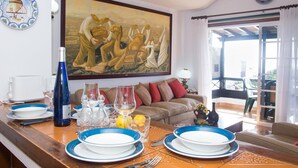 Un coin repas avec une table dressée pour deux personnes, un tableau accroché au-dessus de la table et une vue sur l’extérieur par une porte vitrée.