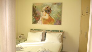 Un lit bien fait, avec du linge de lit blanc et deux oreillers, une table de chevet avec une lampe, et un tableau accroché au-dessus du lit.