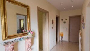 Un couloir avec un grand miroir, une console en verre agrémentée d’éléments décoratifs roses, et une porte ornée d’un petit élément décoratif mural.