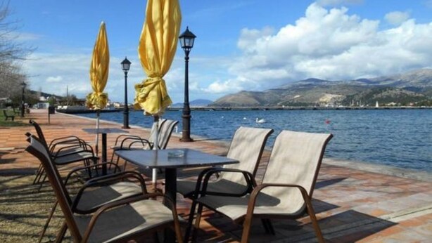Un espace extérieur aménagé avec des tables et des chaises, des parasols jaunes et une vue sur l’eau et les montagnes.