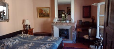 A bedroom with a bed, a fireplace, a desk, and a chair.