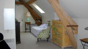 A bedroom with a sloped ceiling, a bed, a dresser, and a lamp. - Chevannes: House with character (Chevannes)