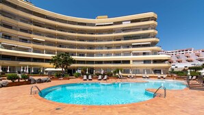A multi-story hotel with a central swimming pool surrounded by lounge chairs and umbrellas. - Santa Maria 99 - One Bed (Costa Adeje)