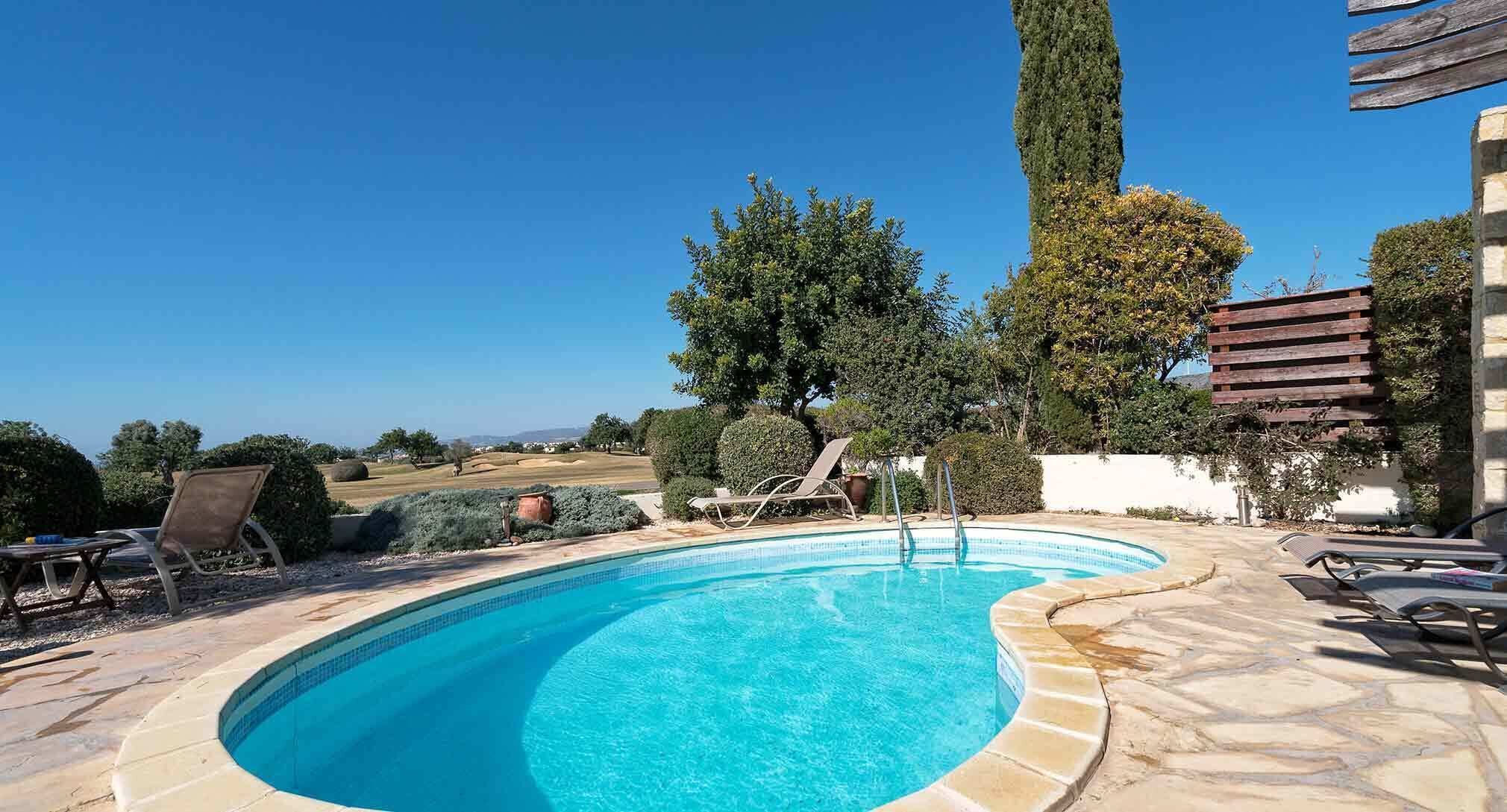 Una piscina con borde curvo, rodeada de sillas de descanso y una terraza de piedra.