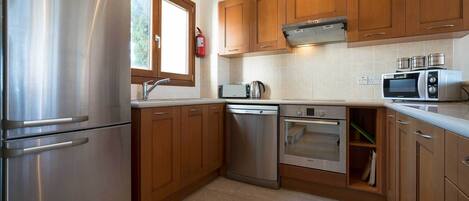 A compact kitchen with stainless steel appliances, wooden cabinets, and a window providing natural light.