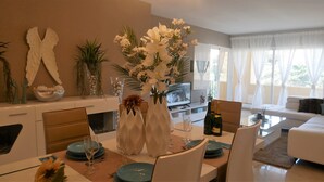 Una sala de estar moderna con comedor, que incluye un televisor de pantalla plana, un sofá y una mesa de comedor con platos, vasos y un centro de mesa.