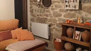 A cozy room with a stone wall, a wooden ceiling, a wooden table with pottery, and a sofa with a blanket.
