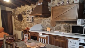 A rustic kitchen with stone walls, wooden furniture, and basic appliances.