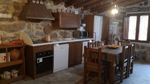 A rustic kitchen with stone walls, wooden beams, a sink, a microwave, and a dining area with chairs and a table.
