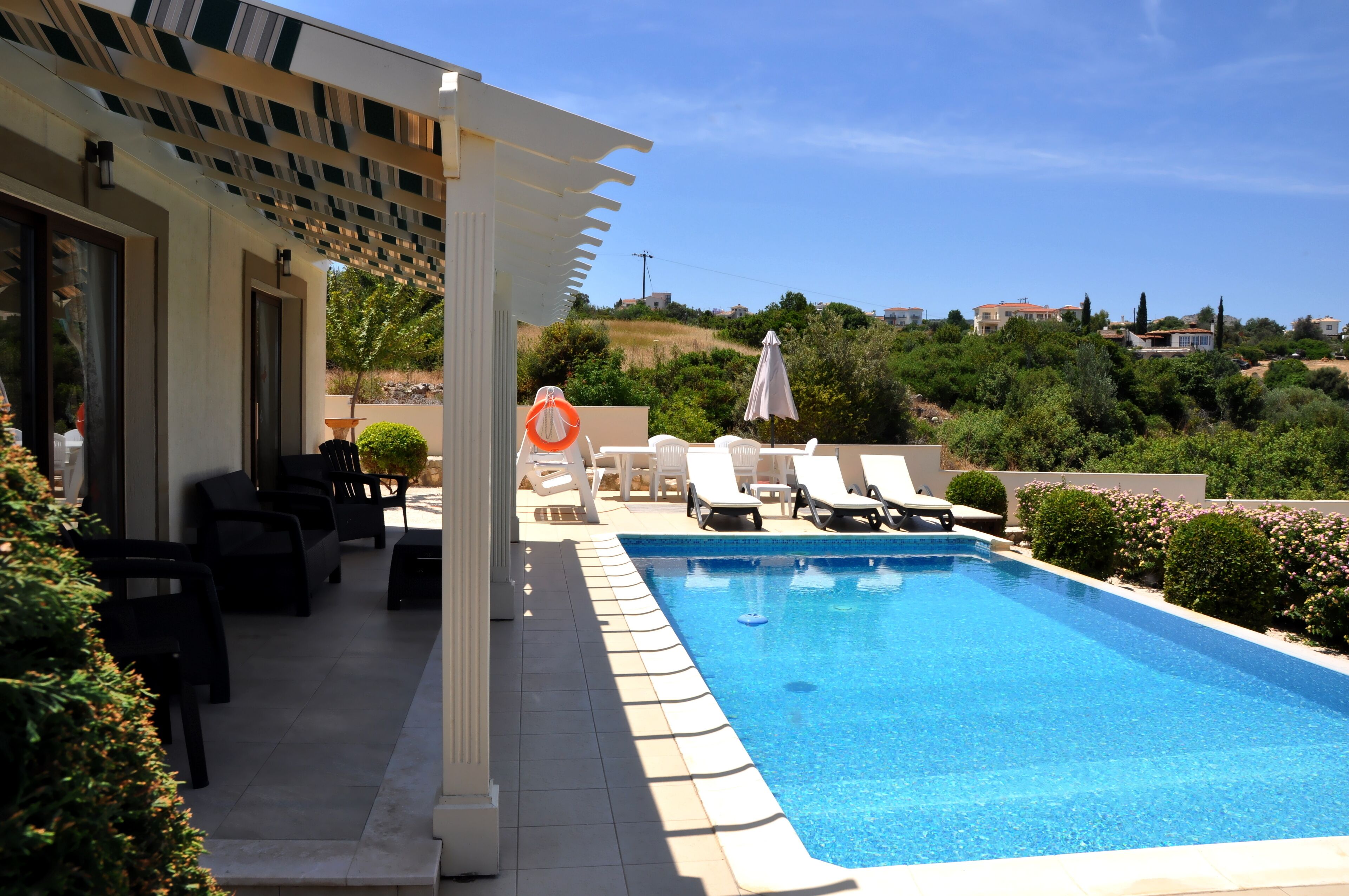 Une piscine entourée de chaises longues et de parasols, bordée de verdure et offrant une vue sur les maisons au loin.