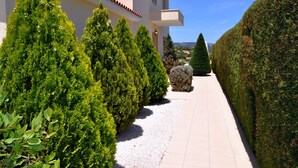A pathway flanked by neatly trimmed hedges and a building with a tiled roof and white walls. - Indulge Yourselves! Perfect Location ~ Private Pool ~ Spectacular Panorama (Neo Chorio)