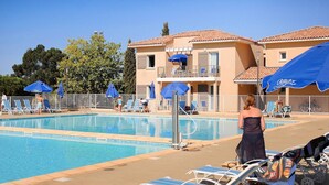 A swimming pool with lounge chairs and umbrellas, surrounded by a building with balconies. - Apartment in France with Pool & Pine Views (La Londe les Maures)