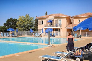 Ein Swimmingpool mit Liegestühlen und Sonnenschirmen, umgeben von einem Gebäude mit Balkonen.