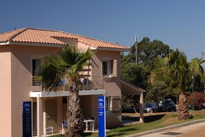 Un edificio de dos pisos con balcón, palmeras y un letrero que indica que es un hotel.