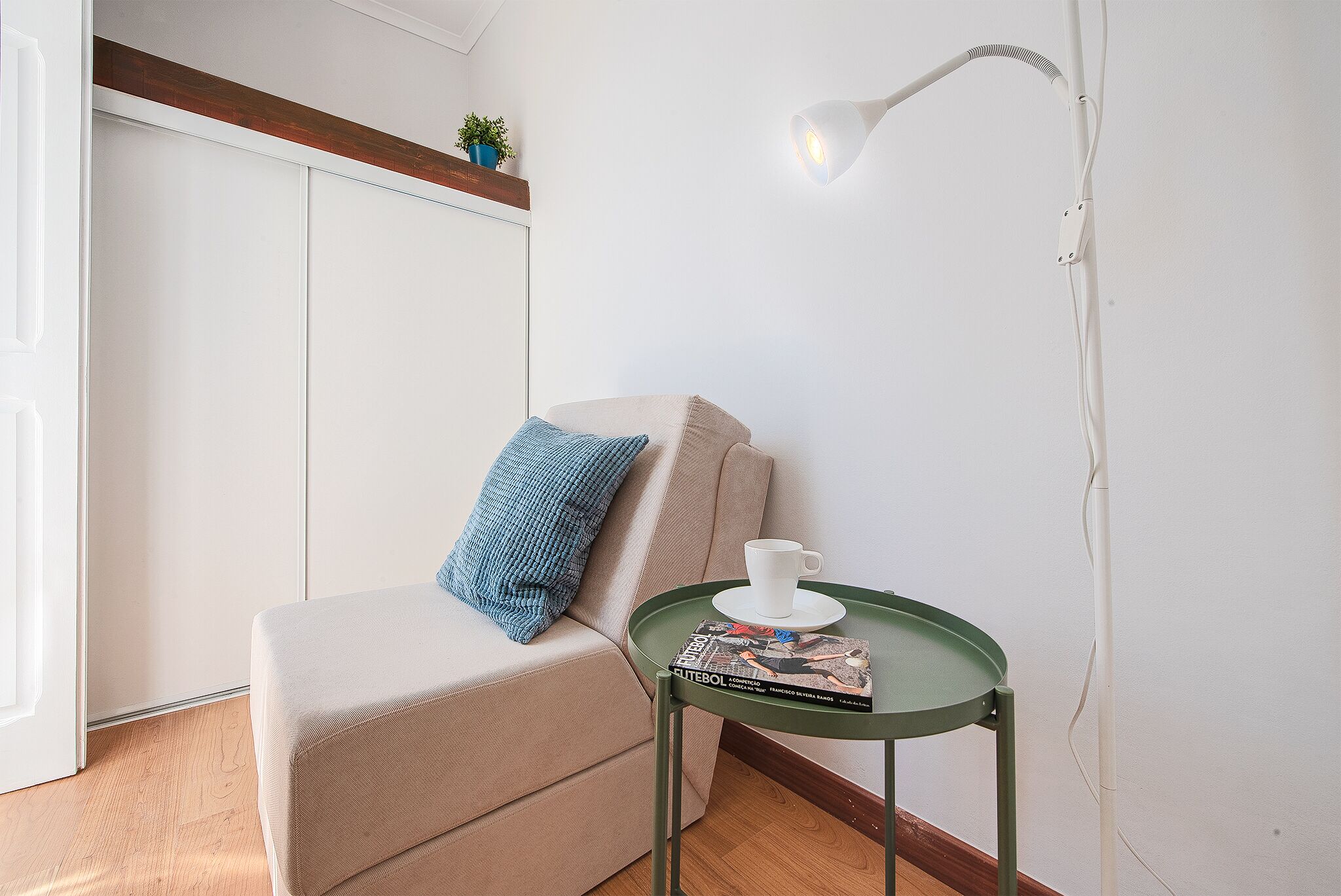 Una habitación con un sofá beige, una almohada azul, una mesita con una revista y una lámpara blanca.