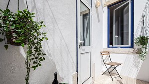 Un petit balcon avec un pot de fleurs en osier, une chaise pliante, une bouteille de vin et un verre posés sur une table verte.