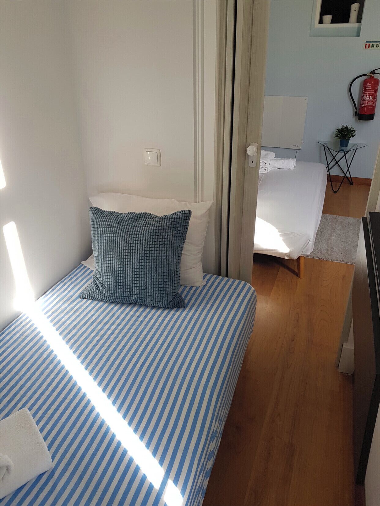 Ein Schlafzimmer mit einem Bett, einem Fenster, einer Tür und einem kleinen Tisch mit einer Pflanze.