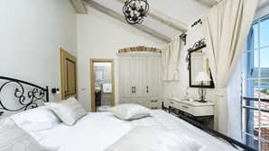 Ein Schlafzimmer mit einem großen Bett, einem Schminktisch, einem Spiegel und einem Fenster mit Vorhängen.