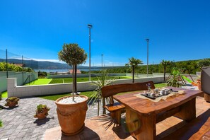 An outdoor patio with a wooden table and chairs, surrounded by potted plants and a view of a landscaped area with a pool and distant mountains. - Villa Mek ZadarVillas (Pridraga)